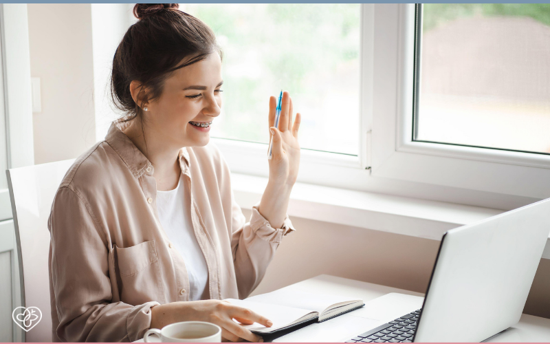 woman sitting down at laptop happy doing telehealth